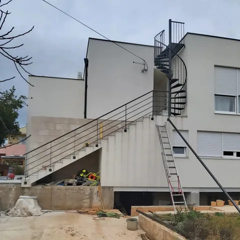 Crno spiralno vanjsko stubište do ravnog krova bijele kuće