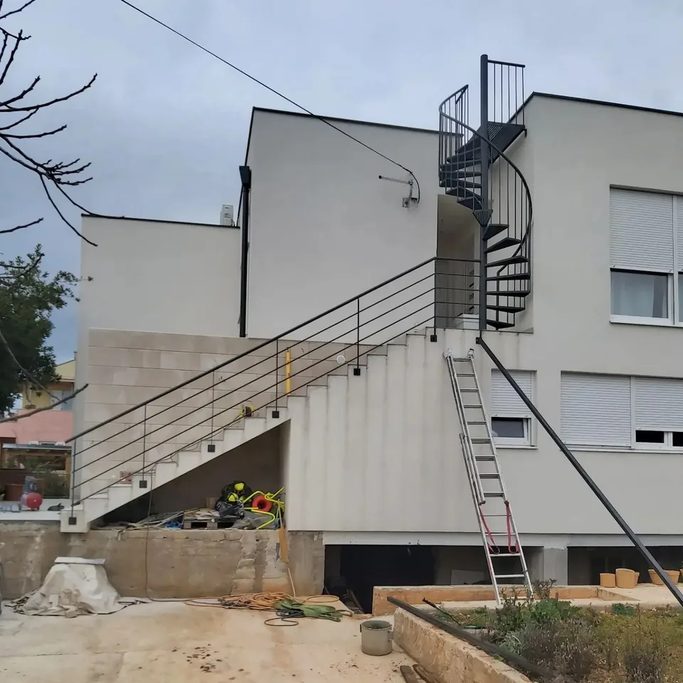 Crno spiralno vanjsko stubište do ravnog krova bijele kuće