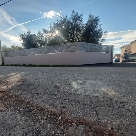 Perforirani sivi paneli ulične ograde i masline iza parapeta