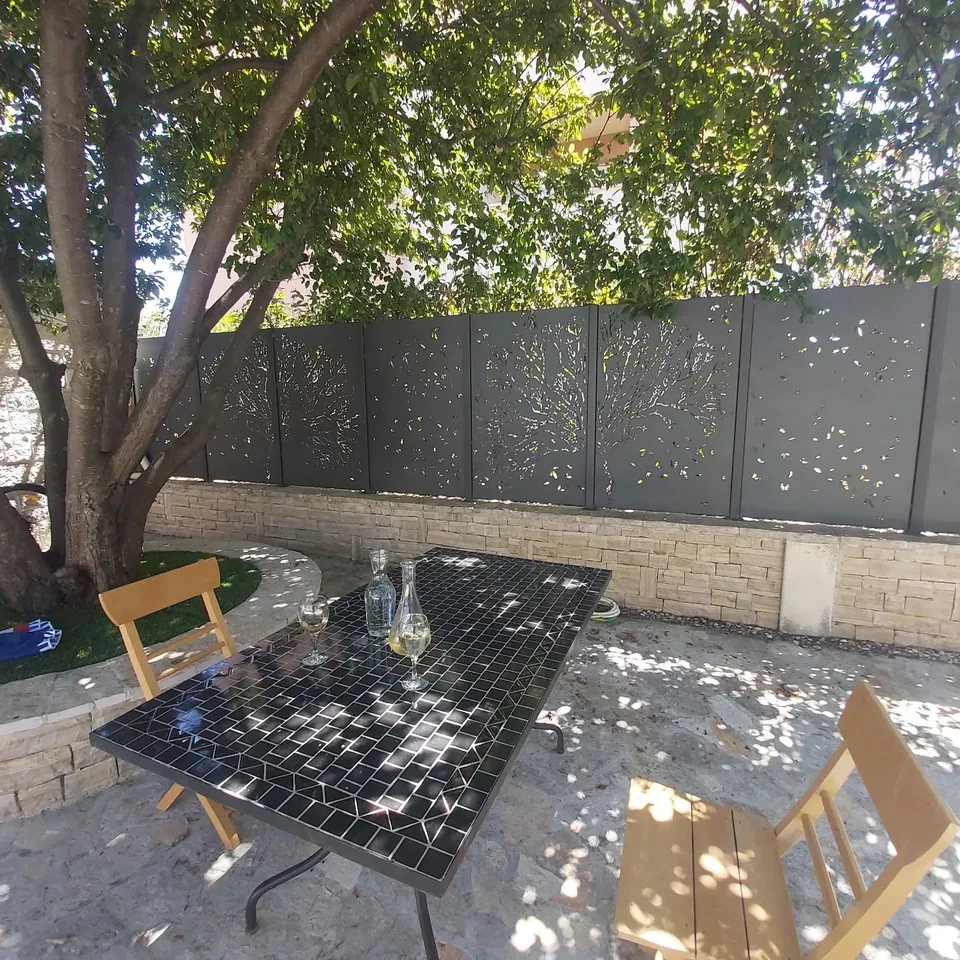 Vrt s tamnim panelima ograde s motivom stabla i kamenim parapetom