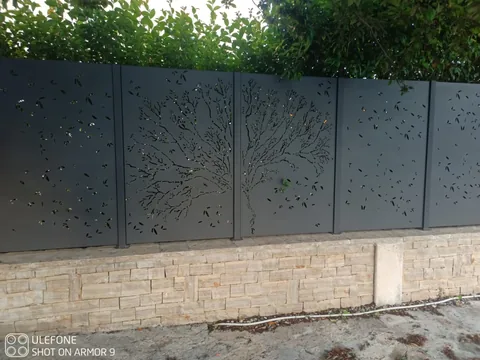 Tamni paneli ograde s rezanim motivom stabla i listova na kamenom parapetu