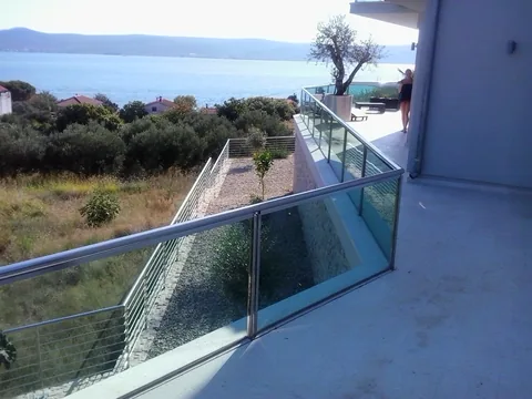 Staklena ograda terase s pogledom prema moru i maslini u posudi