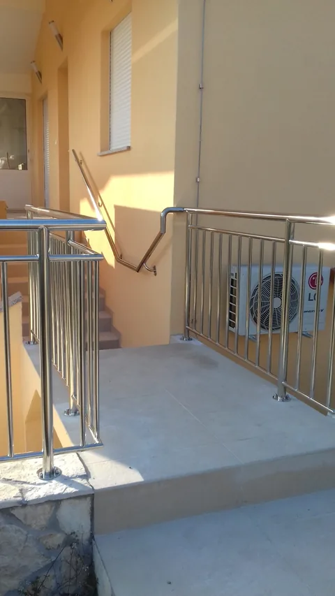 Ulaz uz žutu fasadu s okomitom inox ogradom i zidnim rukohvatom