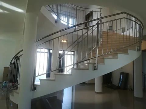 Zakrivljeno svijetlo stubište s inox ogradom i okruglim bijelim stupovima