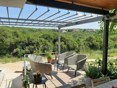 Metalna pergola nad terasom s vrtnom garniturom i pogledom na zelenilo